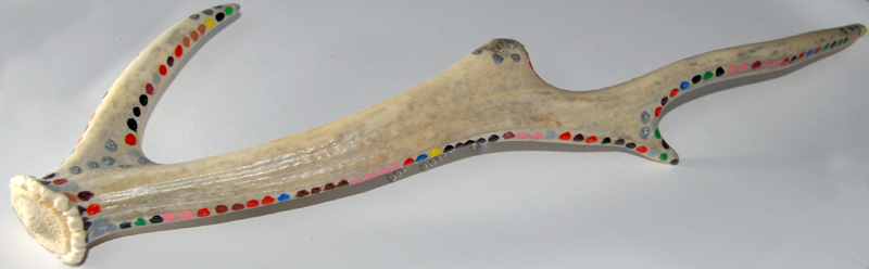 Colour photograph of an antler, painted with coloured dots encircling it.