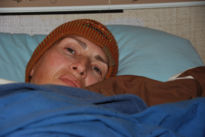 Colour photograph of me in bed, with just my face in a woolen hat looking out