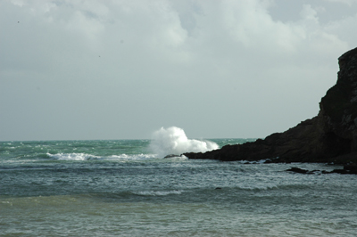 Colour photograph of waves breaking over the end of a headland, with calmer water in the foreground.