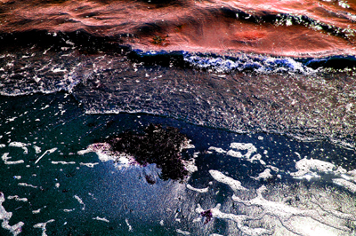 Digitally manipulated photograph of a wave retreating on sand, coloured in red.
