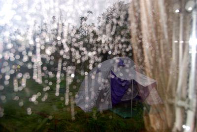 Colour photograph of a small silver and purple tent, viewed through rain on a window