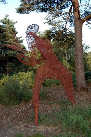 Colour photograph of a large wicker sculpture of a figure setting a bird free, surrounded by woodland.