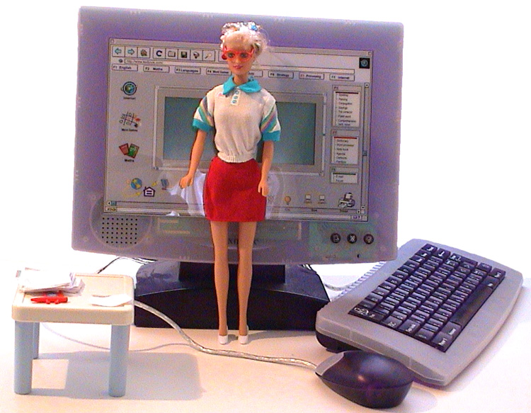 Eine Modepuppe in Rock, Bluse und rote Brille vor einem weissen Hintergrund. Hinter ihr ist ein Kinder-Computer und ein Puppen-Tisch mit Papier und Kugelschreiber.