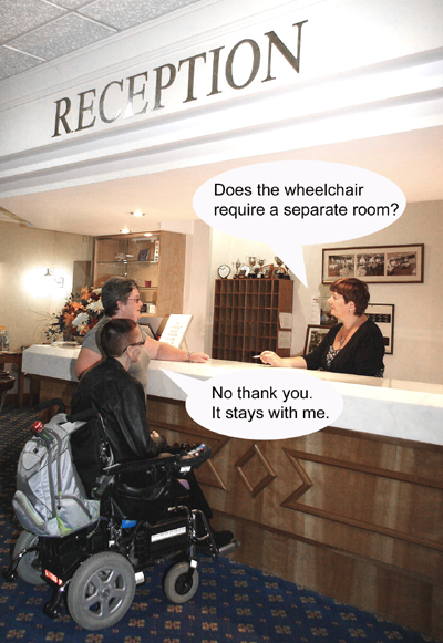 Colour photograph showing a wheelchair user and her companion at a hotel reception. The receptionist is asking the companion: "Does the wheelchair require a separate room?" and the wheelchair user is replying instead: "No thank you. It stays with me."